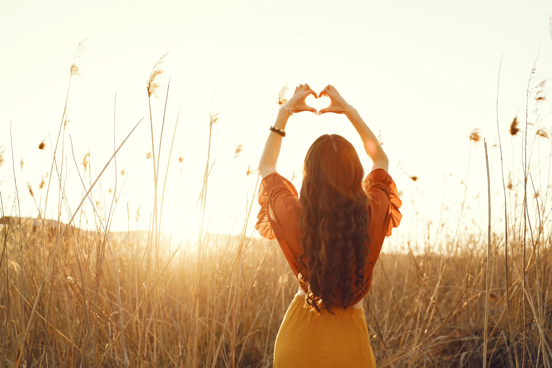 Vrouw die hartje maakt met handen de zon in een veld